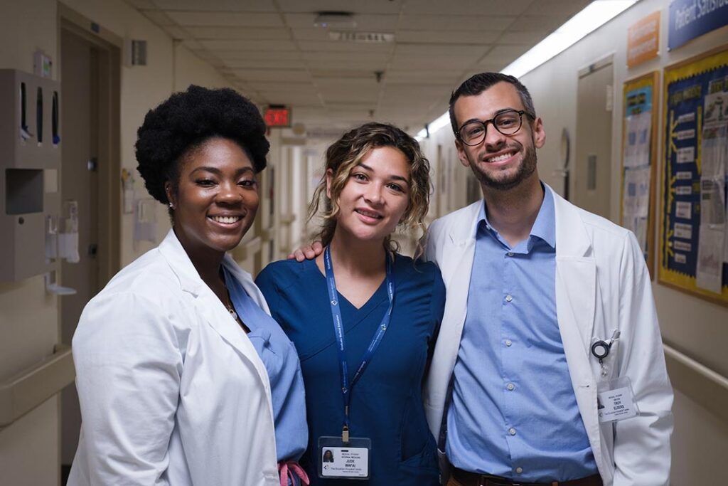 Three smiling medical students standing together in a hospital hallway