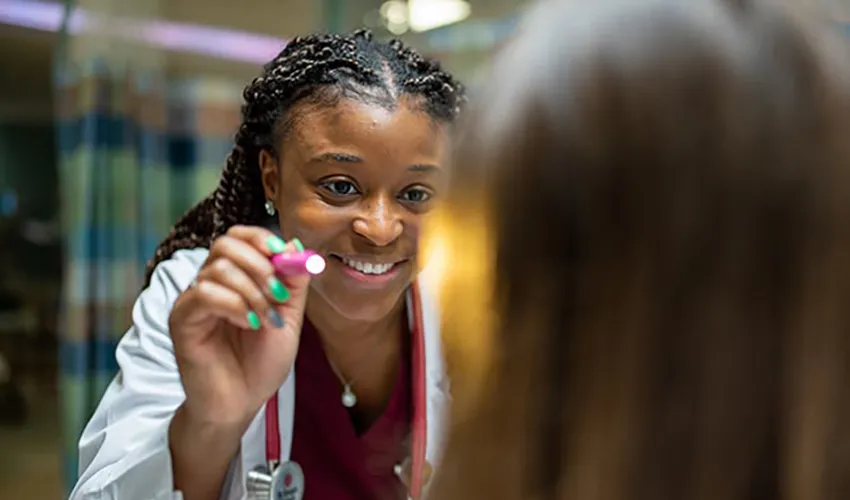 Smiling doctor in a white coat examining a patient with a penlight News