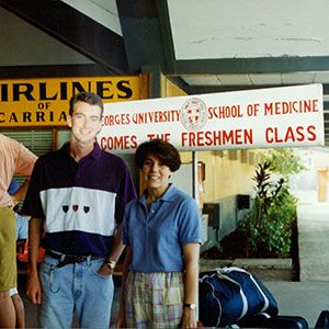 Two students posing with luggage beside a St. George’s University School of Medicine freshman welcome banner