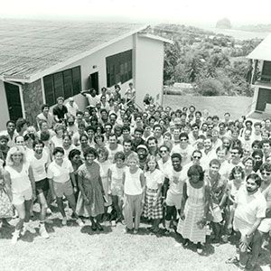 Large group of people posing together outside near hillside buildings in a black-and-white photo