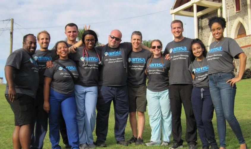A diverse group of smiling SGU medical students wearing AMSA shirts poses together during a community outreach event.