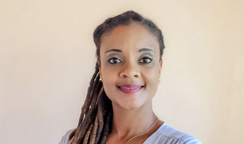 Smiling woman with dreadlocks swept over one shoulder against a plain background