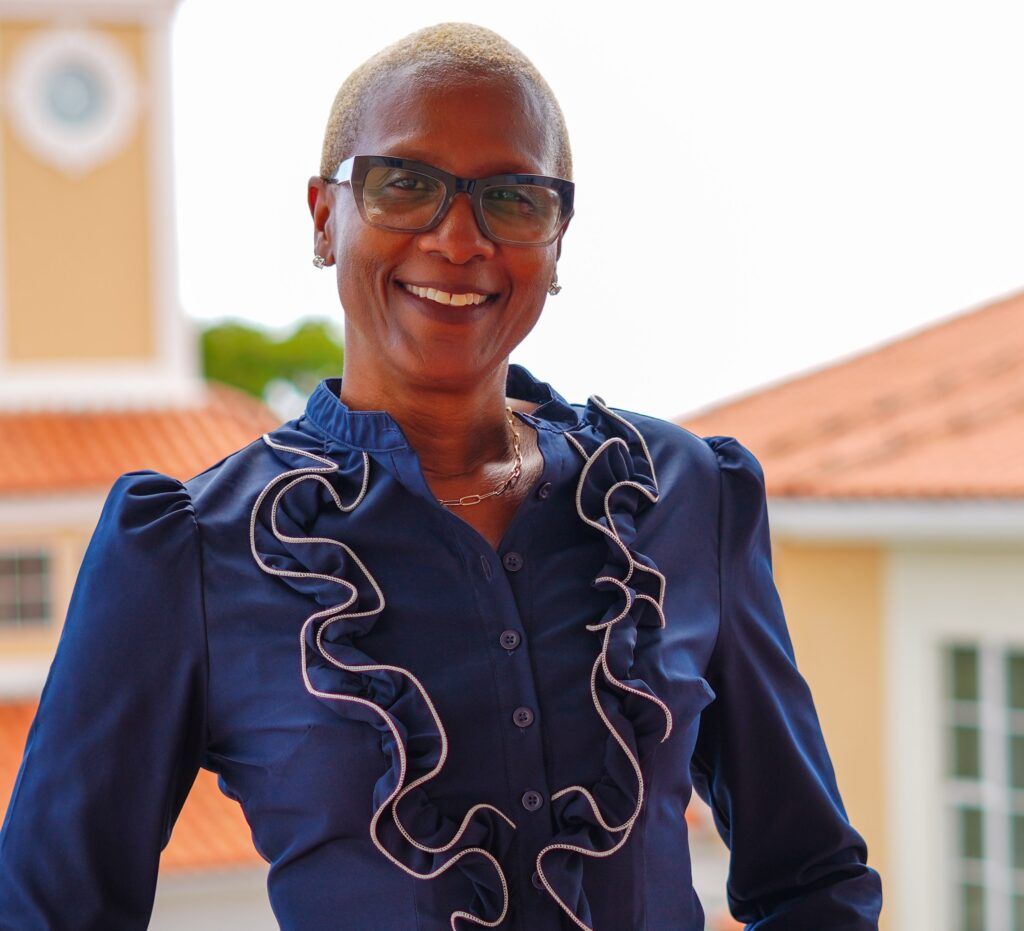 Smiling woman with short blonde hair and glasses wearing a navy blue ruffled blouse