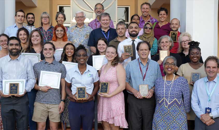 A group of attendees and award recipients posing together outdoors with certificates and plaques