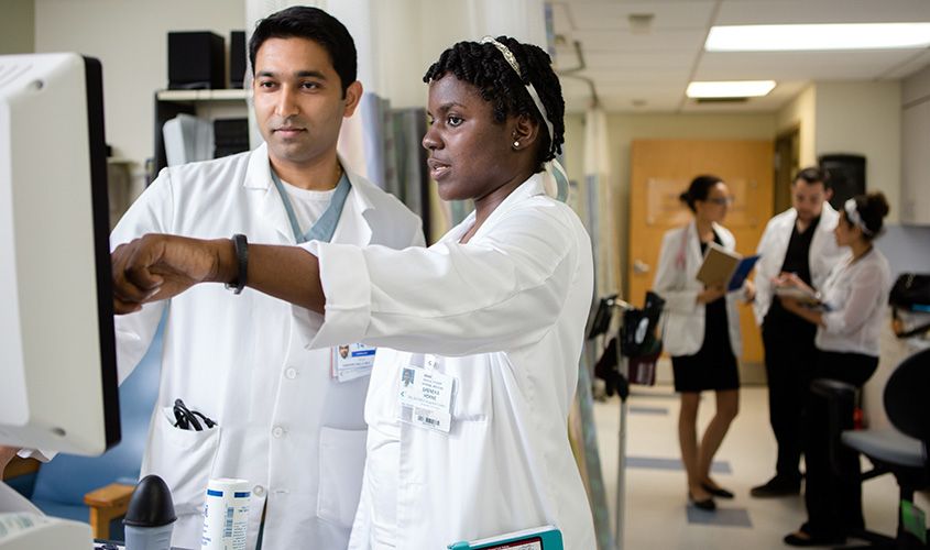 A group of diverse medical students or doctors in white coats posing in a city environment.