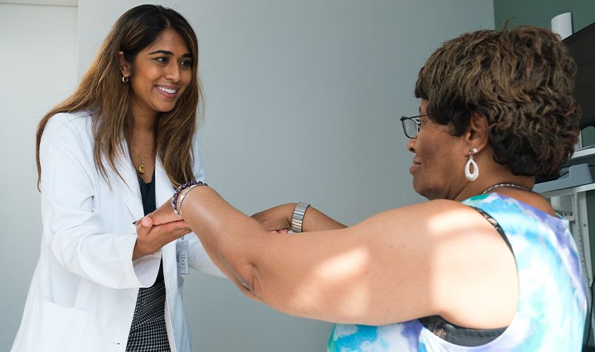 A smiling doctor in a white coat holds and examines a patient's outstretched hands