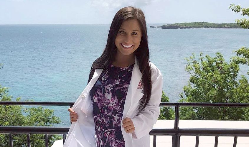 A portrait of Maria Coppola, DVM, an SGU School of Veterinary Medicine student and SGA President, standing outdoors in her white lab gown