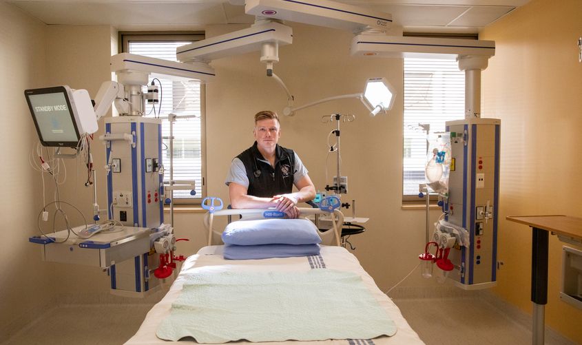 A healthcare worker leaning against an empty hospital bed surrounded by advanced medical equipment