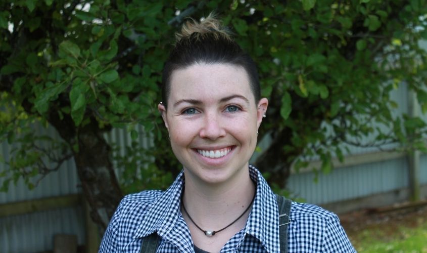 Smiling person with hair tied in a bun, wearing a checkered shirt outdoors
