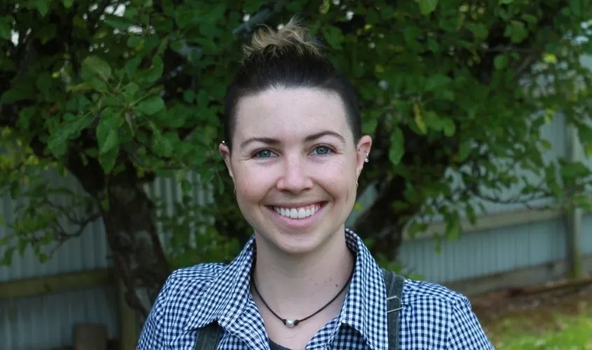 Smiling person with hair tied in a bun, wearing a checkered shirt outdoors News