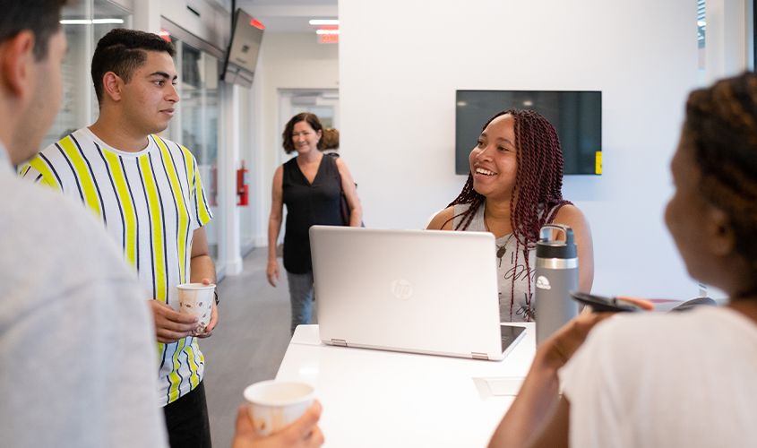 Colleagues smiling and talking around a laptop at a modern standing desk News