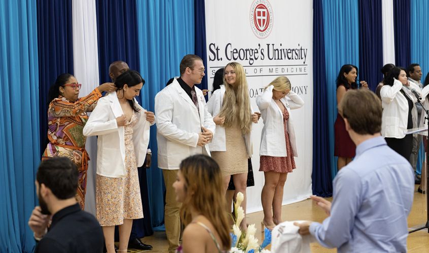 Medical students putting on their white coats on stage during a St. George's University White Coat Ceremony News