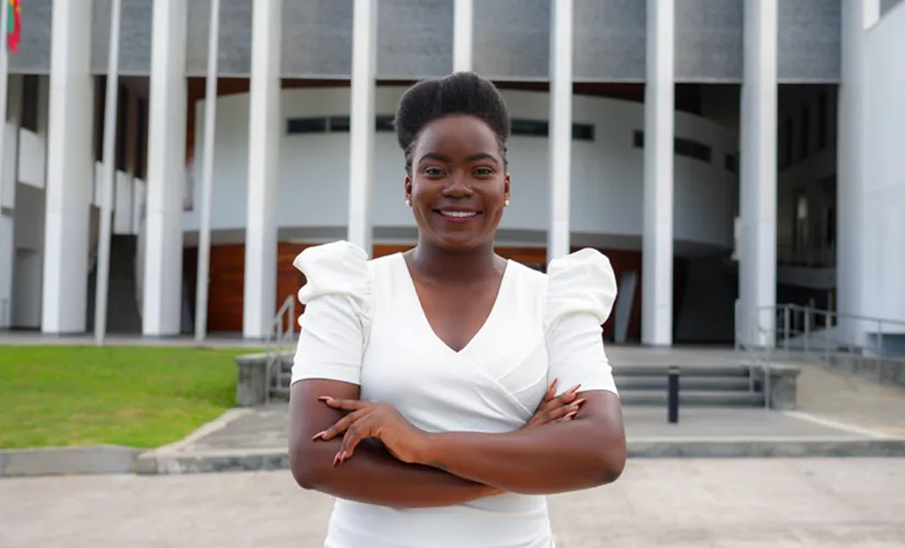 Smiling woman in a white dress with arms crossed, standing outside a modern building with large columns