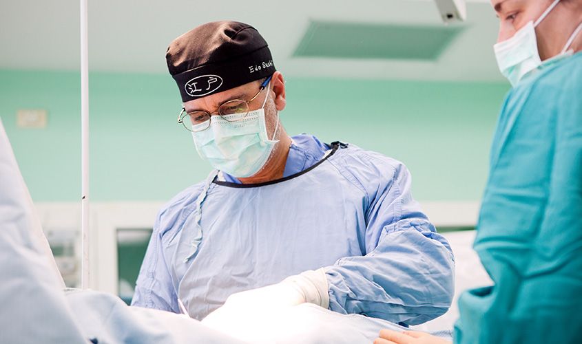 Interventional cardiologist Dr. Mark Lanzieri wearing scrubs and a surgical cap while performing a procedure in a hospital operating room