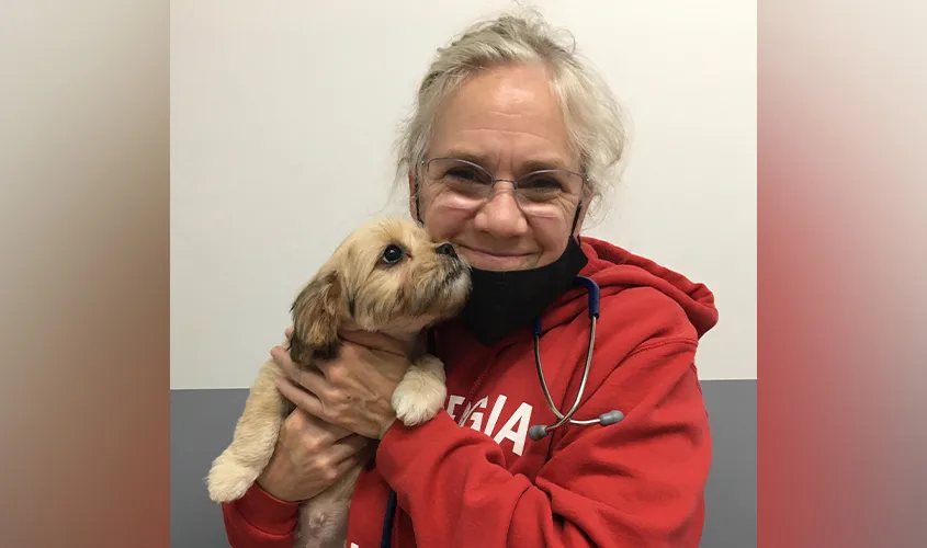 Dr. Laura Boggs, SGU DVM '12 alumnus and relief veterinarian, smiling while affectionately holding an adorable puppy in a clinic.