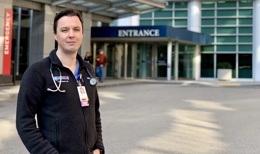 A doctor wearing a fleece jacket and stethoscope standing outside a hospital emergency entrance News