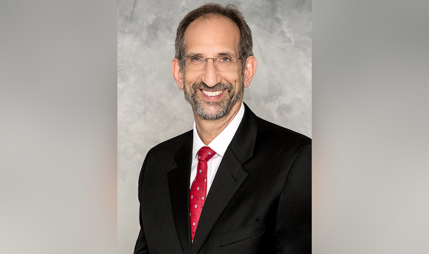 Smiling man with glasses and a beard wearing a black suit and red tie in a professional portrait