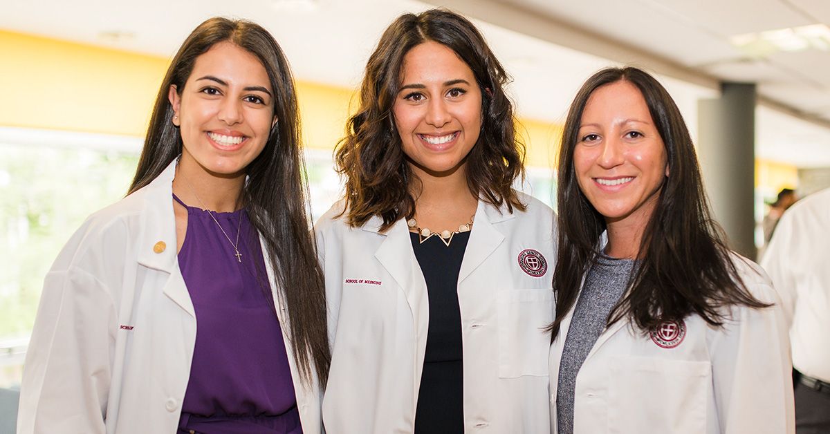 Three female medical students or physicians in white lab coats smiling during an event. News