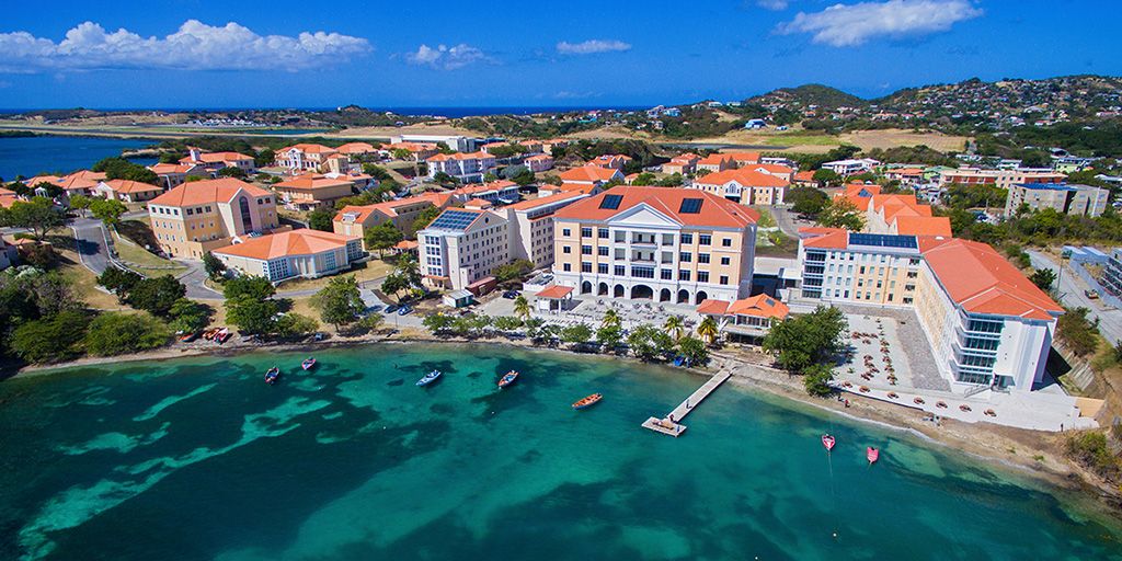 Aerial view of a coastal campus with terracotta-roofed buildings along a turquoise bay with small boats and a dock News