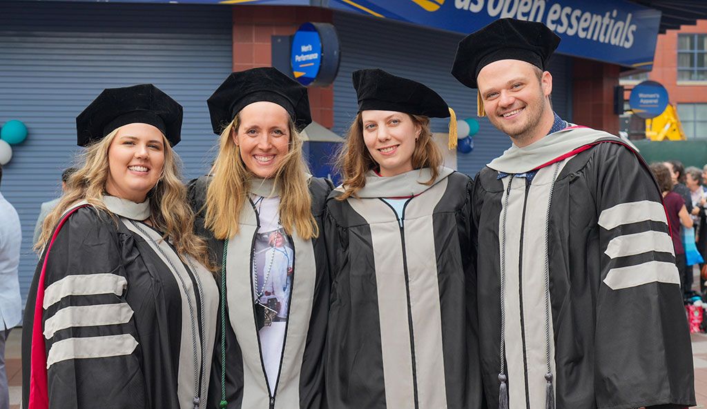 Four smiling graduates standing together in doctoral regalia and caps