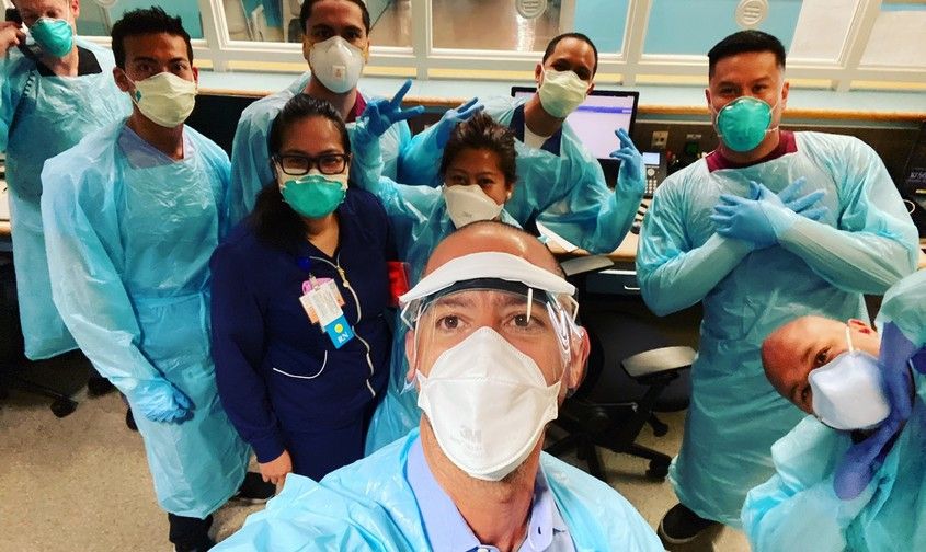 Healthcare workers posing together wearing protective gowns, face masks, and gloves in a hospital setting