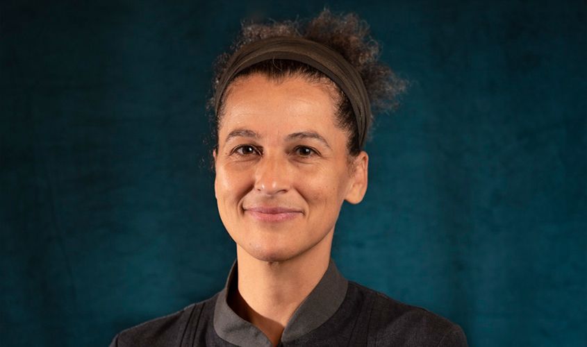 Smiling woman with curly hair pulled back in a headband against a dark teal background