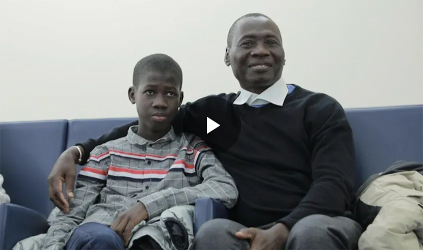 A smiling man sits with his arm around a young boy on blue seating News