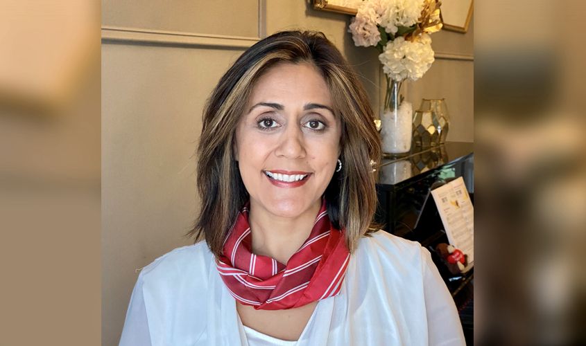 Smiling woman with shoulder-length brown hair wearing a white top and a red striped scarf News