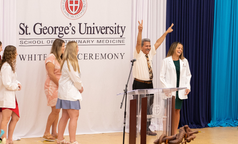 A speaker and students celebrate on stage at a St. George's University School of Veterinary Medicine white coat ceremony News