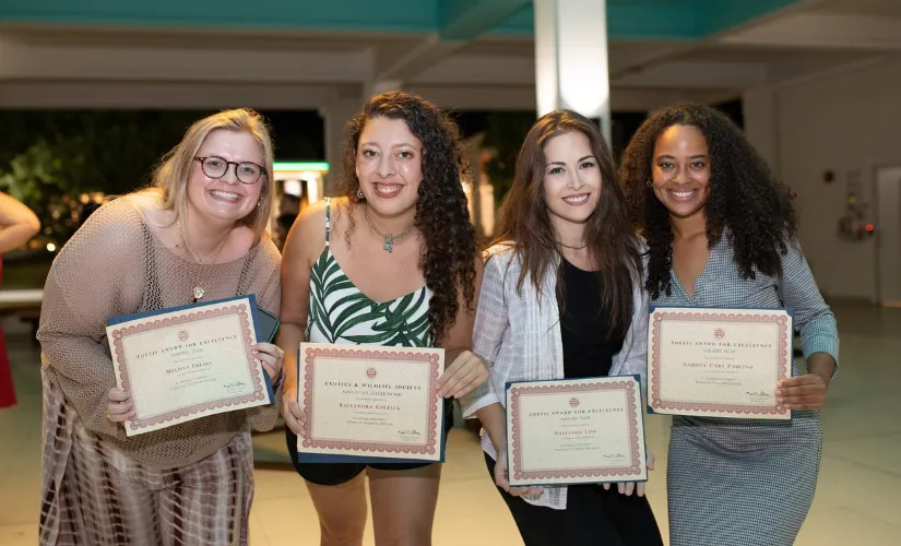 Four smiling women holding up award certificates together at an evening event