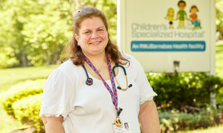 Smiling healthcare worker wearing a stethoscope outside a Children's Specialized Hospital sign News