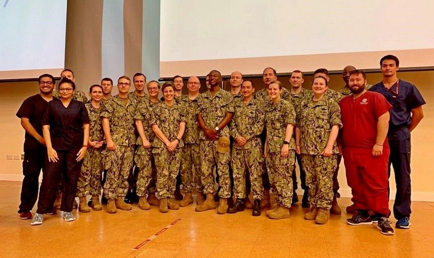 Large group of U.S. military personnel in Navy camouflage uniforms posing with medical students, related to the USNS Comfort mission.