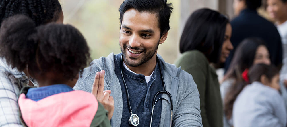 A medical volunteer smiles while helping a mother and young child.]