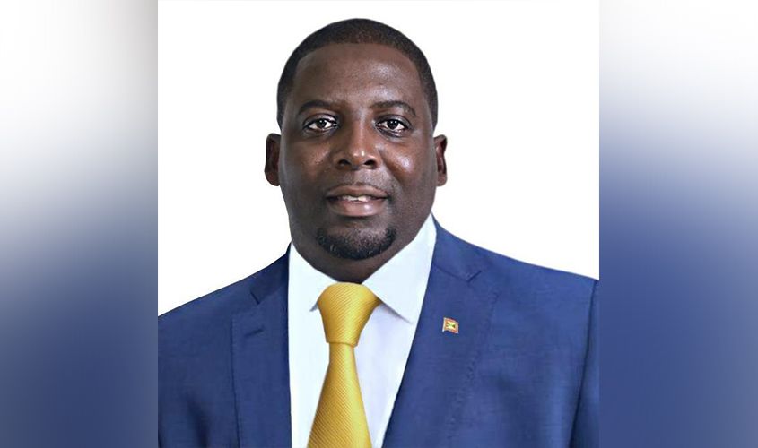 Dickon Mitchell in a blue suit and yellow tie wearing a Grenada flag lapel pin