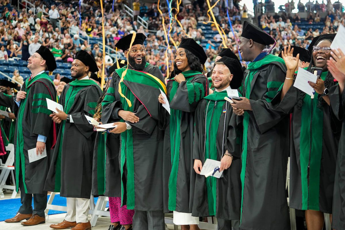 Graduates in black and green academic regalia celebrate as streamers fall during a commencement ceremony