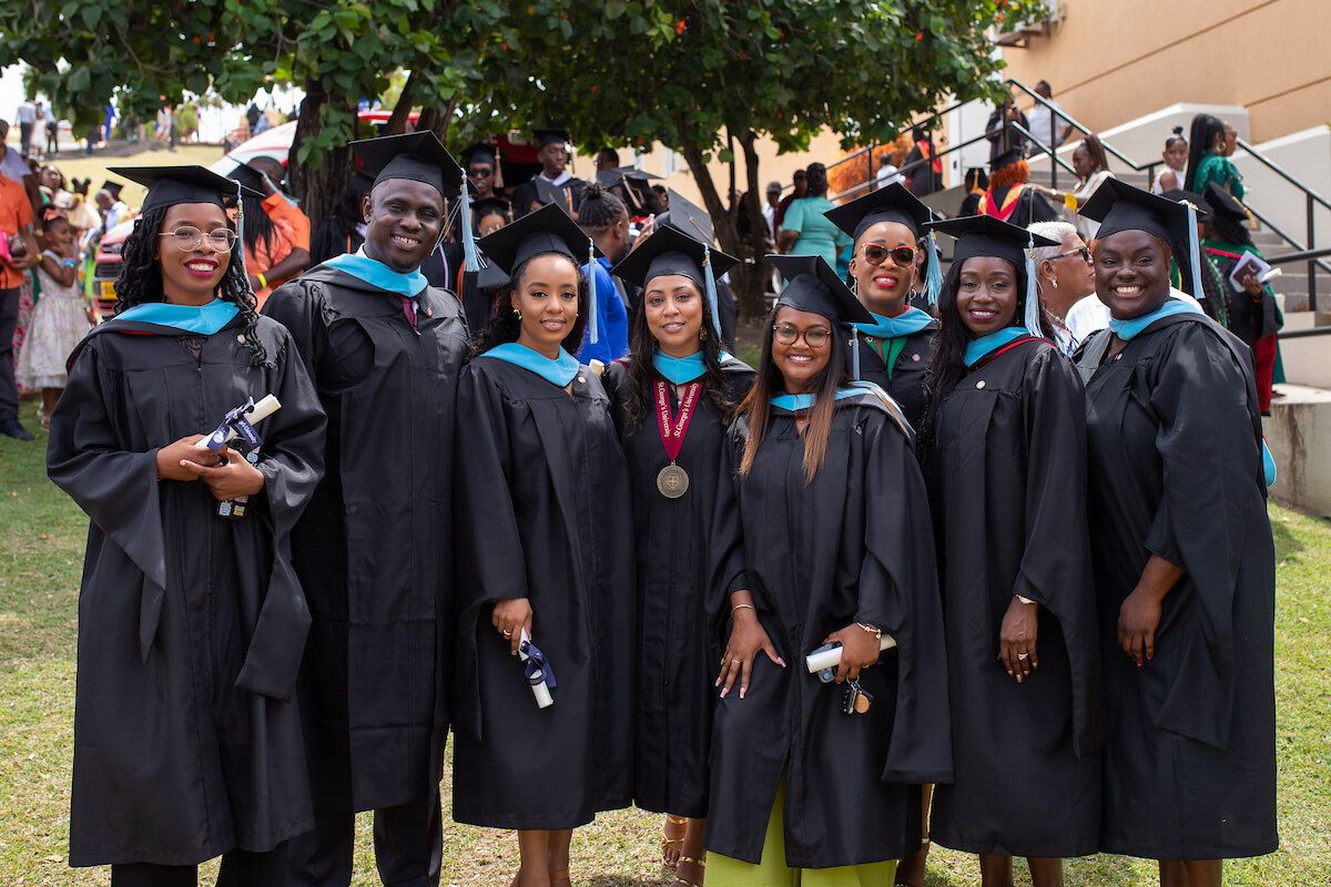 Smiling graduates posing together outdoors in academic caps and gowns during a graduation ceremony