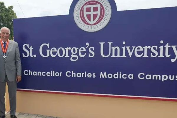 Charles Modica wearing a medal standing next to the St. George's University Chancellor Charles Modica Campus sign