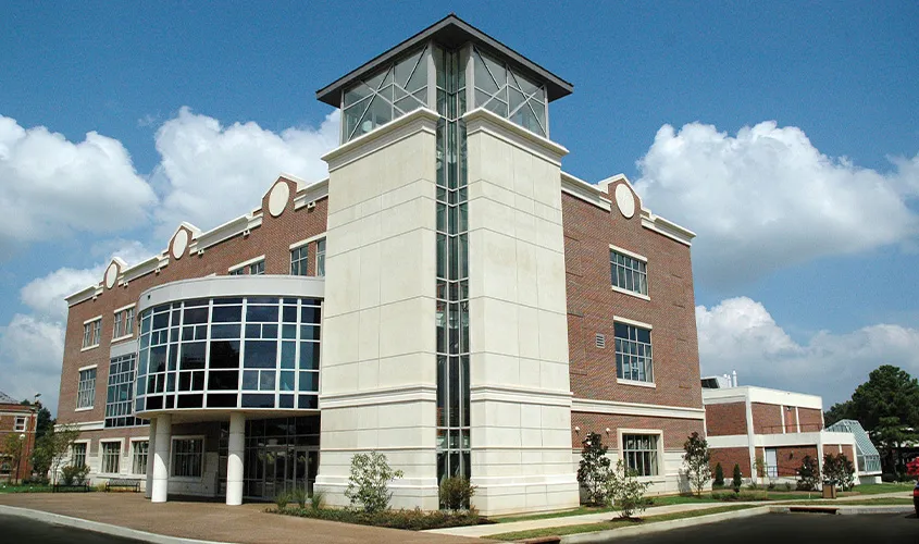 Modern multi-story brick building featuring a tall white stone tower and a curved glass entrance