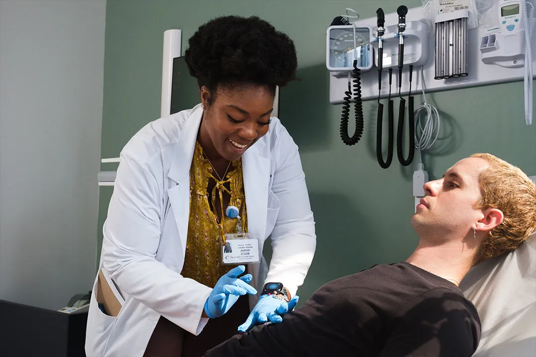 A smiling doctor in a white coat conducts a physical exam on a patient lying on a clinic examination table