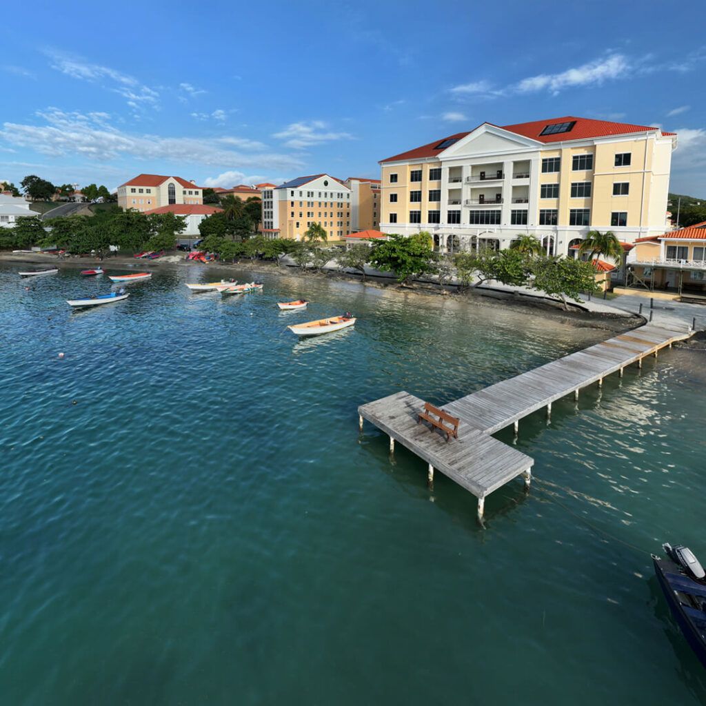 Wooden dock with a bench extending into turquoise water near small boats and waterfront buildings
