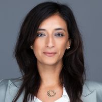 Professional headshot of a woman with long dark hair wearing a light gray blazer against a solid gray backdrop