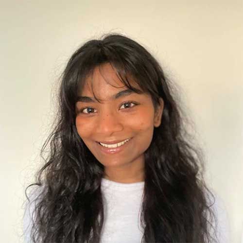 Smiling young woman with long dark wavy hair and bangs wearing a white shirt
