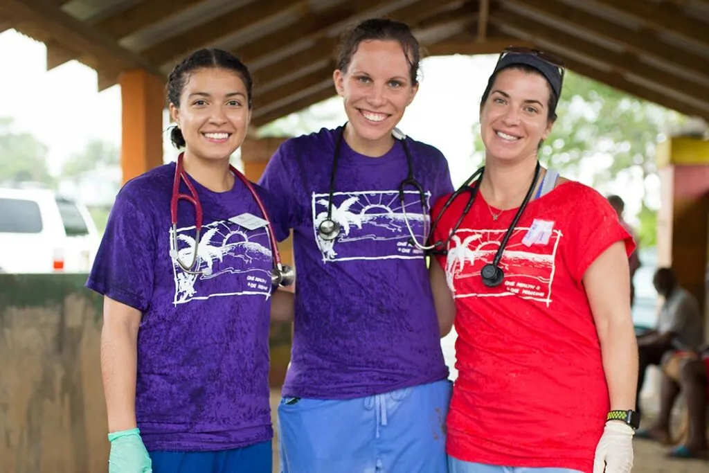 Three smiling healthcare volunteers wearing stethoscopes and matching One Health shirts