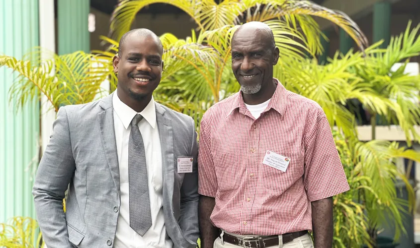 Two smiling Ministry of Agriculture officials standing together outdoors in front of palm plants