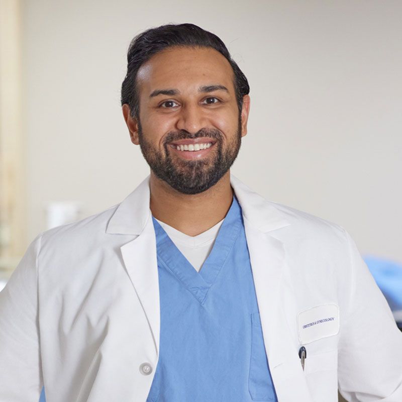 Smiling male doctor with a beard wearing blue scrubs and a white lab coat