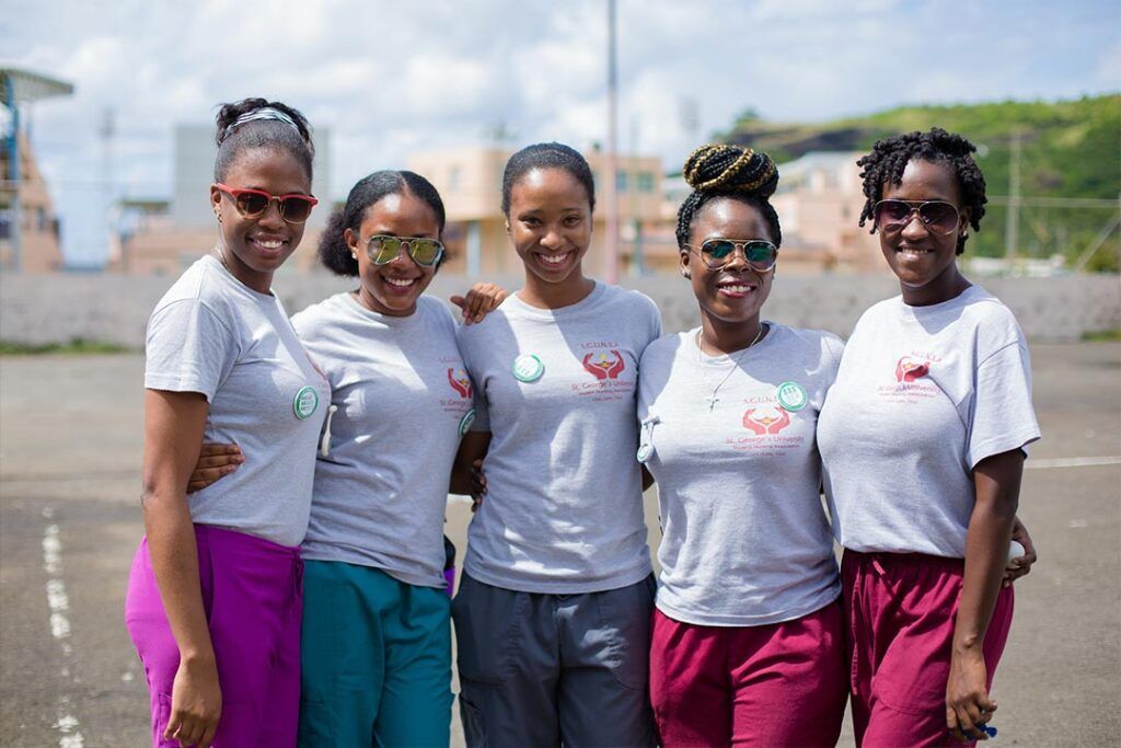 Five smiling St. George's University nursing students in matching shirts and scrubs posing together outdoors