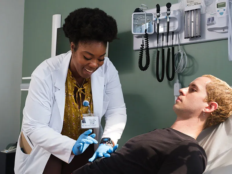 A smiling doctor wearing a white coat and gloves examines a patient lying on an exam table