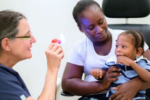 An eye doctor uses a light-up toy to examine a young child sitting on a woman's lap