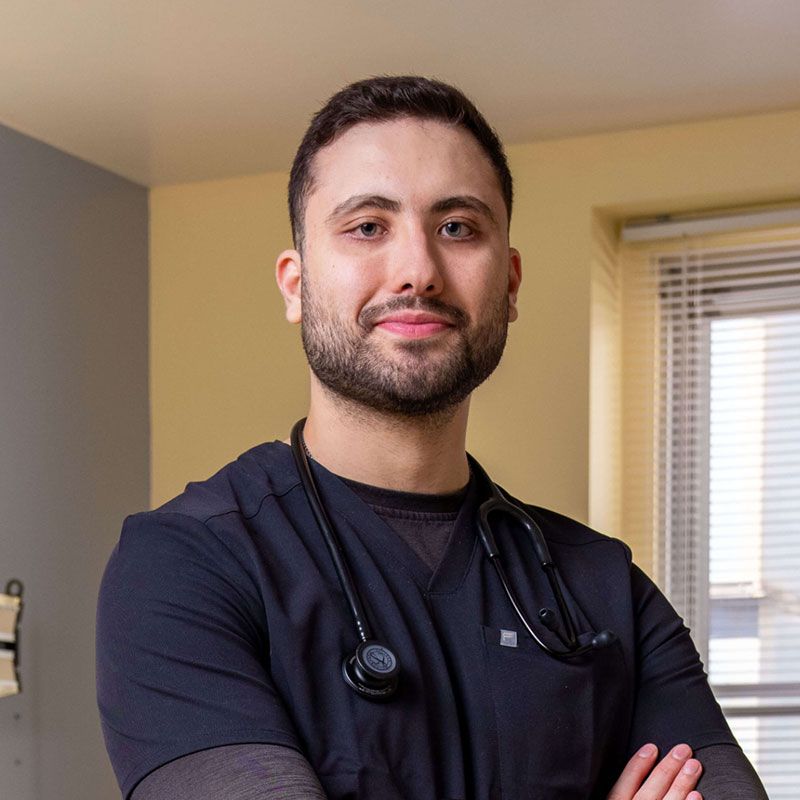 Male healthcare worker with a beard wearing black scrubs and a stethoscope around his neck
