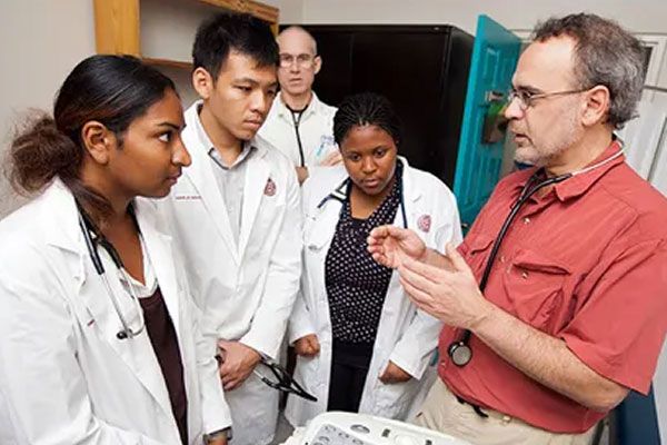 A doctor instructs a group of medical students wearing white lab coats and stethoscopes